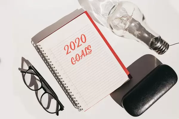 Top view of office desk with glasses and notebook with 2020 goals. New year concept.