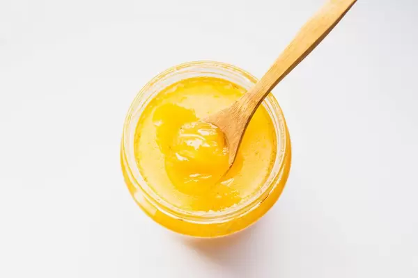 Top view of organic honey in a glass jar with wooden spoon on white background