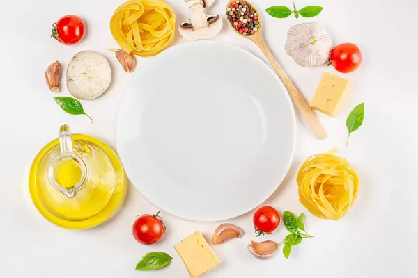 Top view of pasta, raw vegetables and spices on white background with empty plate in the middle