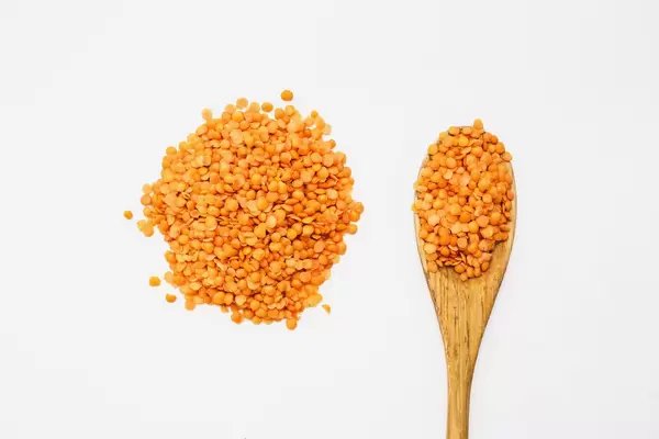 Top view of red lentils on a wooden spoon on white background