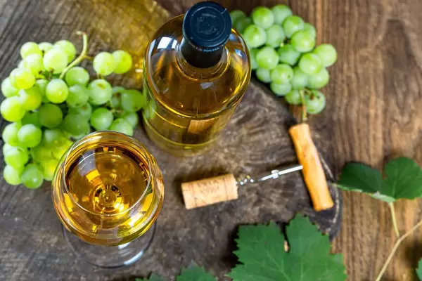 Top view of ripe grapes and white wine in bottle and glass on old wooden background