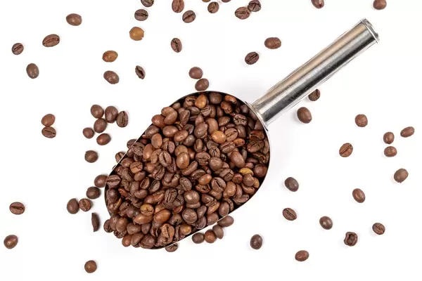 Top view of roasted coffee beans in metal scoop on white background
