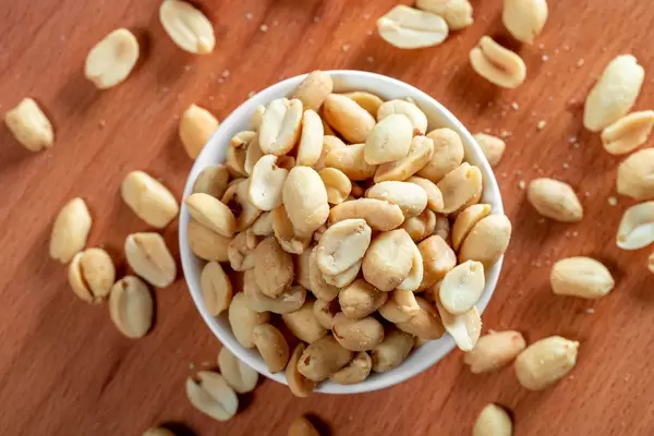 Top view of roasted peanuts in white ceramic bowl on wooden background (Flip 2019)