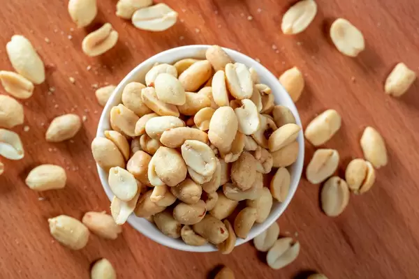 Top view of roasted peanuts in white ceramic bowl on wooden background