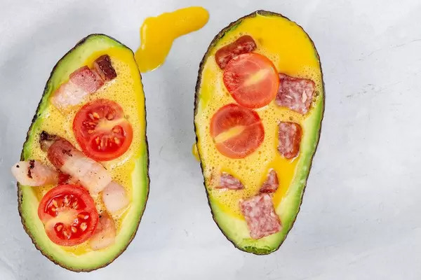 Top view of sliced Avocado with eggs meat and tomato ready for baking