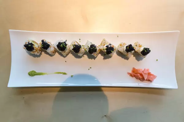 Top view of sliced sushi "Lucky No Fish", with vegan caviar topping, vegan tuna substitute, avocado, spicy sauce, kimchi sesame seeds and spring onions