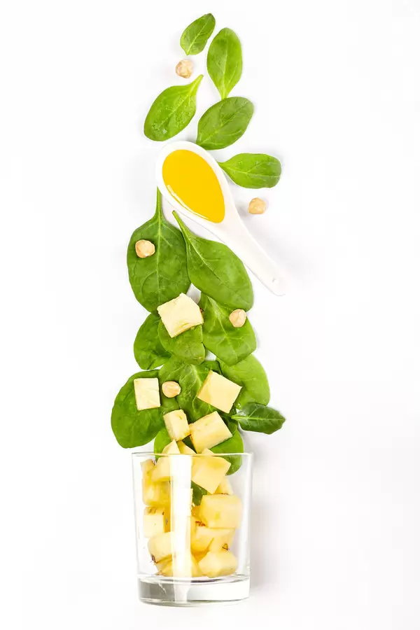 Top view of spinach leaves, honey, pineapple slices, hazelnuts and glass on white