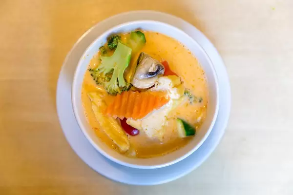 Top view of the "Tom Yum" -  veggie soup with coconut milk, fresh vegetables and hot spices in a white bowl on a wooden table