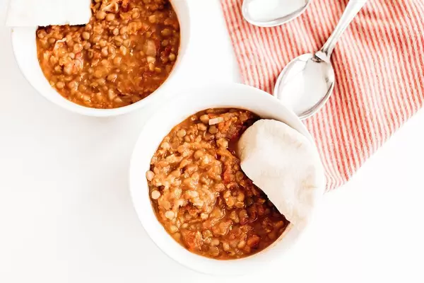 Top view of two bowls of two lentil dahl with pita bread on table