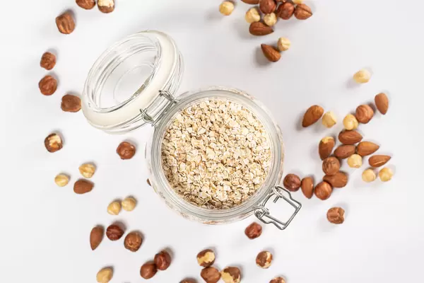 Top view, open jar of oatmeal on white with hazelnuts and almonds