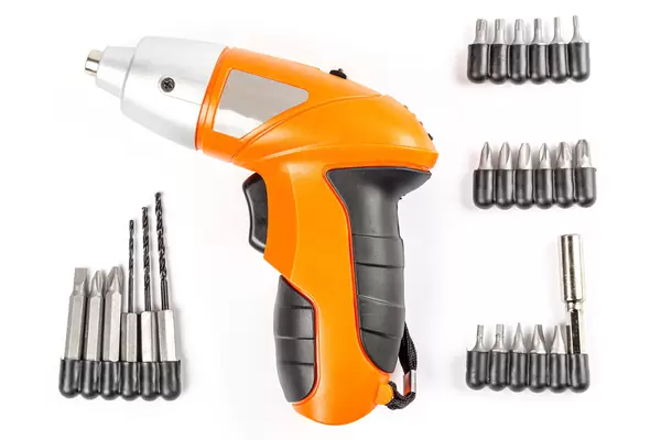 Top view, orange electric screwdriver with bits and drills on white