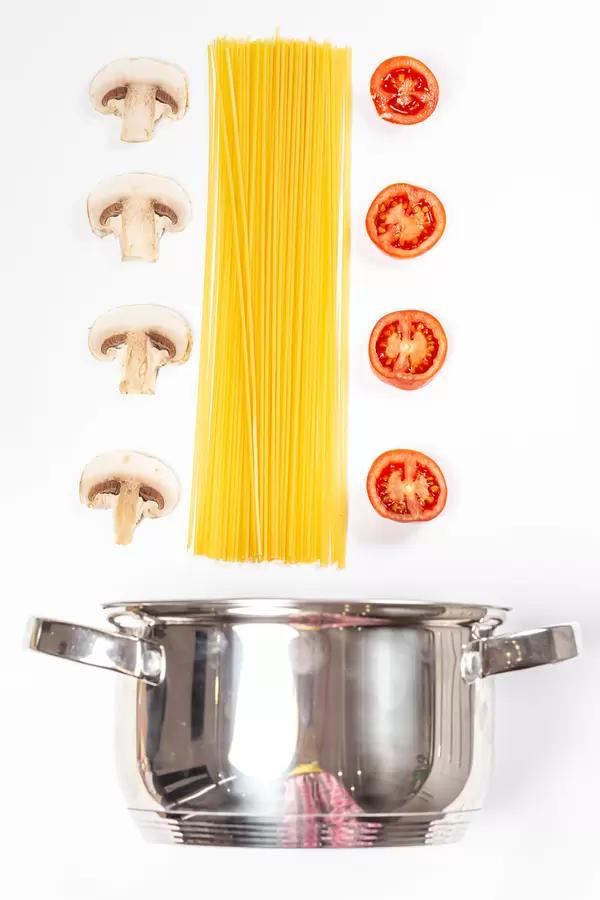 Top view, pan with spaghetti, slices of fresh mushrooms and tomatoes