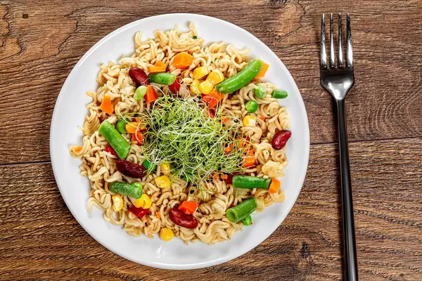 Top view pasta with vegetables on wooden background with fork