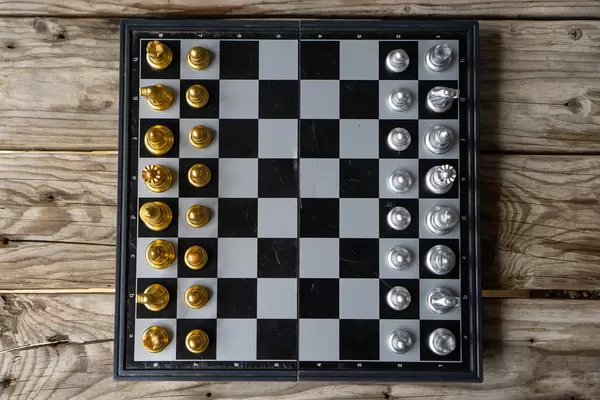 Top View Photo of a Portable Chess Board with Magnetic Chess Pieces in Silver and Gold in Starting Position on a Wooden Table