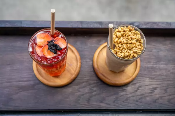Top View Photo of  Milkshake with Puffed Rice Cerals and Strawberry Iced Tea in Cocktail Glasses with Paper Straws on a Wooden Balcony Table at a Cafe