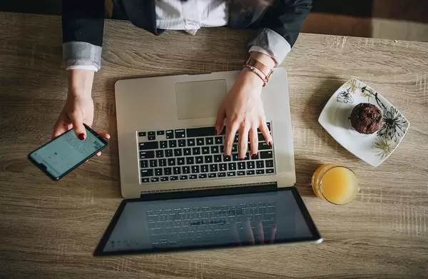 Top View Photo of Person working on Laptop and Smartphone next to Orange Juice and Muffin in a Cafe