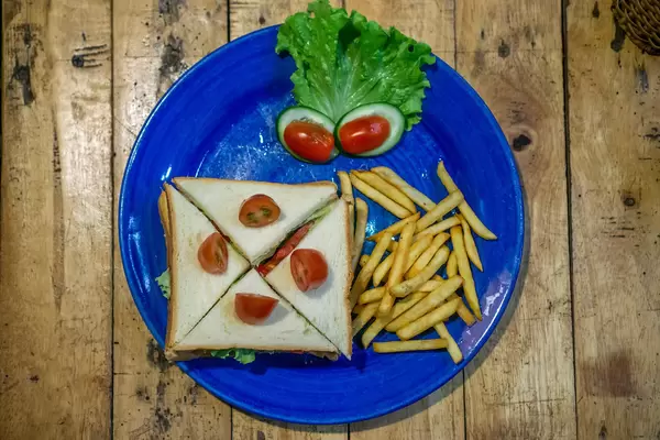 Top View Photo of Quartered Tuna Sandwich with French Fries and Cherry Tomatoes on a Wooden Table.
