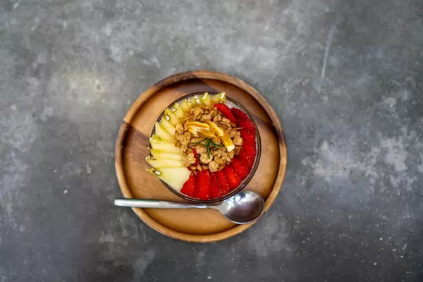 Top View Photo of Sliced Apples and Strawberries in a Glass of Yogurt with Cereals on a Wooden Plate