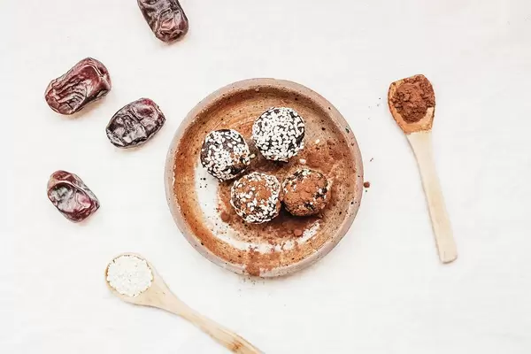 Top View Photo of Vegan Sesame Energy Balls with Cocoa Powder next to Spoons with Sesame and Cocoa Powder and Dates on White Background