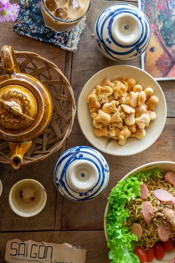 Top View Photo of Wooden Coffee Table with Ceramic Tea Pot, Cookies as Snack and Dried Noodles with Sausage and Lettuce