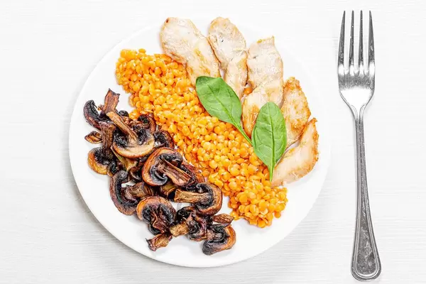 Top view plate with lentils, chicken and mushrooms on a white wooden background