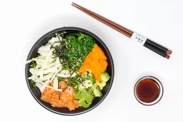 Top view - Poke Bowl Salmon Teriyaki  - with sushi rice, salmon, avocado, cabbage, wakame, wasago, nori, teriyaki-sauce, soy-sauce, sesame and chives in a bowl with chopsticks