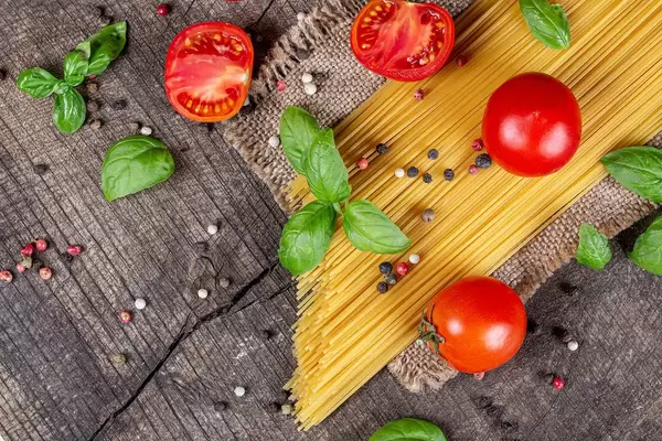Top view, raw spaghetti, tomatoes, basil and spices on old wooden background