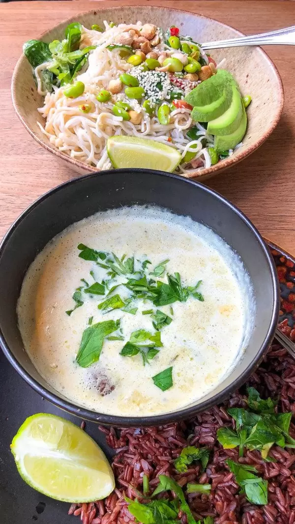 Top view: rice noodles with tamari & ginger dressing, avocado, edamame, peppers, sesame, corn salad, peanuts, mint and lime (served cold) and green curry (spicy) with Kenya green beans, mushrooms, cherry tomatoes and lime served on brown rice