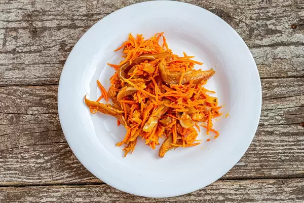 Top view salad with carrots and slices of smoked pork ears in a white plate on an old wooden background (Flip 2019)