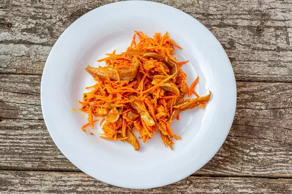 Top view salad with carrots and slices of smoked pork ears in a white plate on an old wooden background