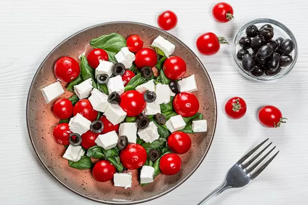 Top view salad with fresh vegetables and feta cheese on white wooden background