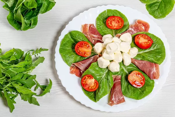 Top view salad with jamon, mozzarella, tomatoes and herbs on a white plate