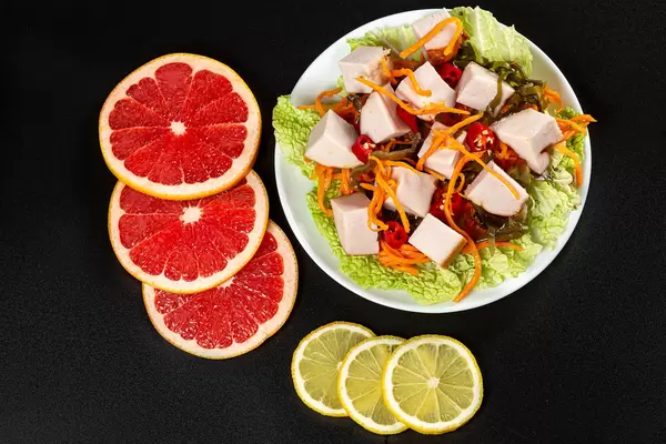 Top view salad with vegetables and chicken on black background with sliced grapefruit and lemon