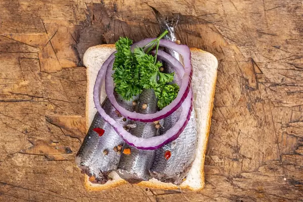 Top view, sandwich with pickled fish, onion slices and parsley on old wooden background