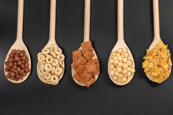 Top view, set of breakfast cereals in wooden spoons on black background