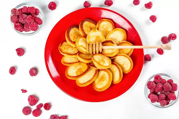 Top view, small pancakes on a red plate with fresh raspberries