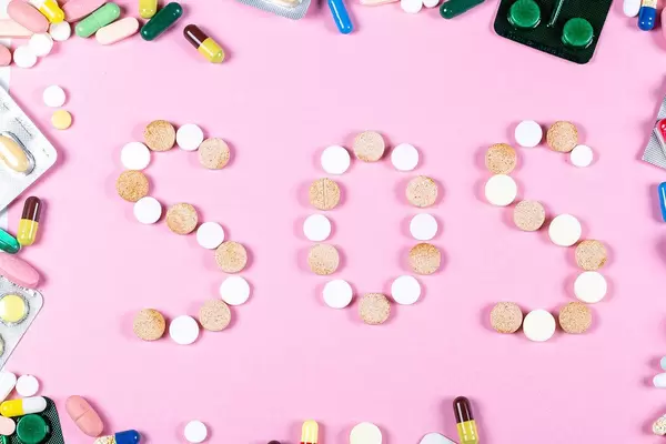 Top view, SOS of tablets on a pink background with a frame of multicolored tablets and capsules