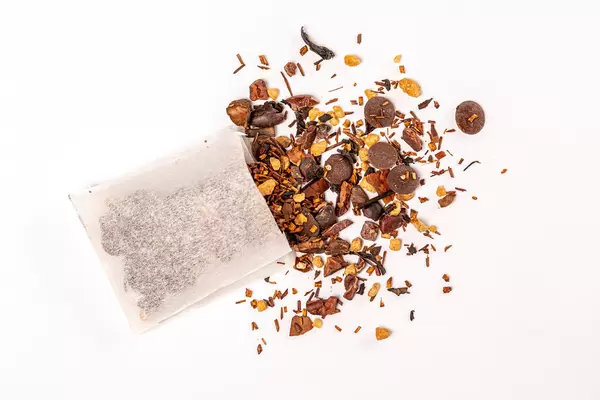 Top view, tea bag with scattered black tea with chocolate and pieces of nuts