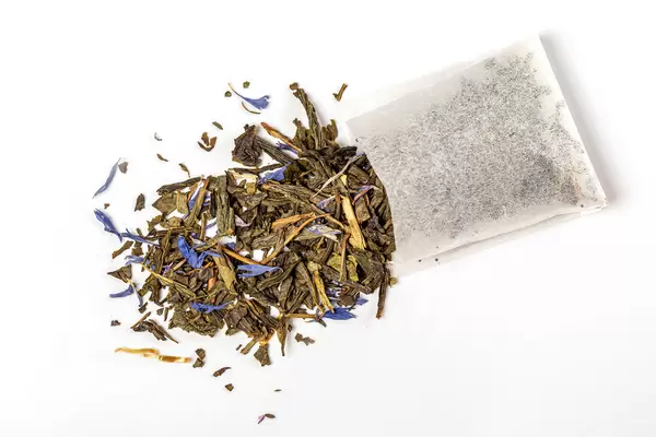 Top view, tea bag with scattered green tea and blue petals