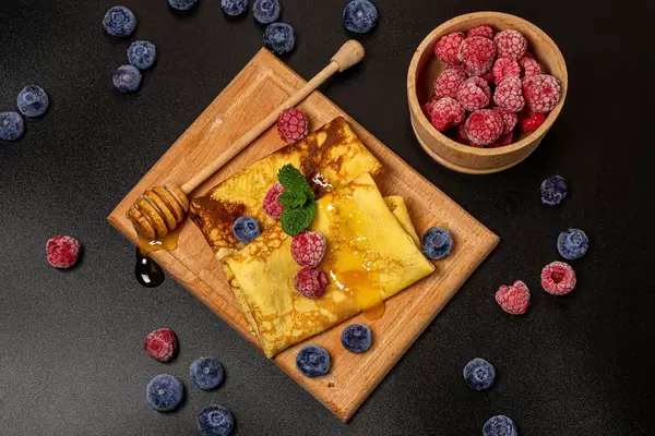 Top view, thin pancakes with berries, mint leaves and honey, dark background