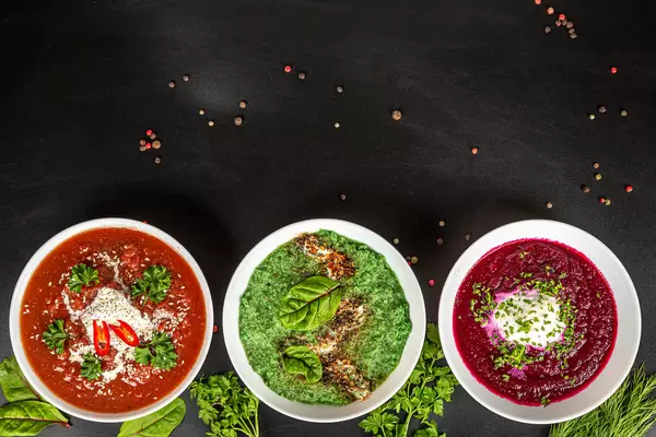 Top view, three bowls with vegetable puree soup on black background