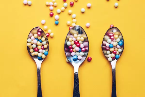 Top view three spoons with colorful sprinkles on yellow background.