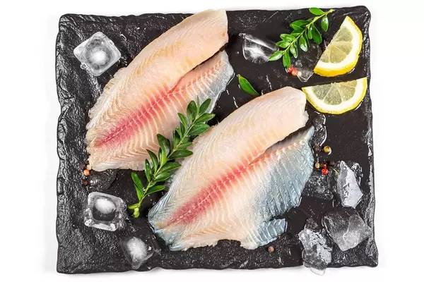 Top view, tilapia fillet with ice and lemon slices on black tray