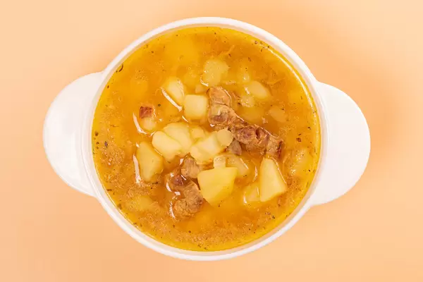 Top view, tureen with potato soup on orange background