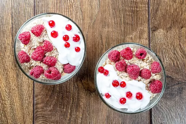 Top view two bowls of oatmeal with fresh berries on a brown wooden background