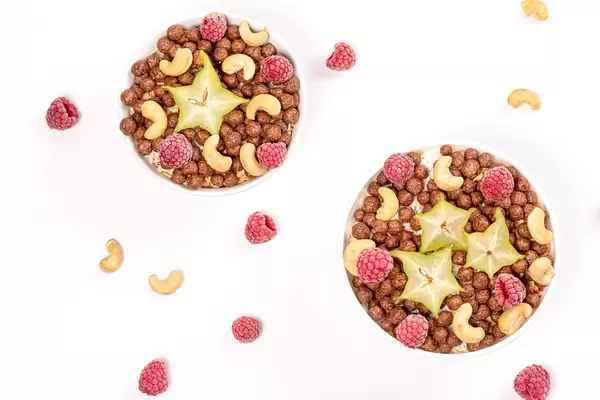 Top view, two bowls with corn balls, cashews, raspberries and caramboli pieces