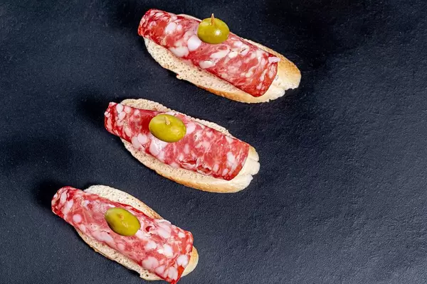 Top-view von Baguette Scheiben mit Salami und grüner Olive auf schwarzem Hintergrund