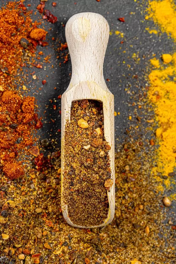Top view wooden scoop with ground pepper mixture on spice background