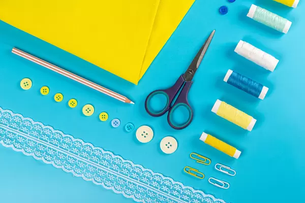 Top view, yellow fabric with threads, buttons and white lace on blue background
