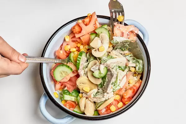 Topf mit frischem Gericht mit Gurken, Champignons, Tomaten, Mais, Fleisch vor weißem Hintergrund